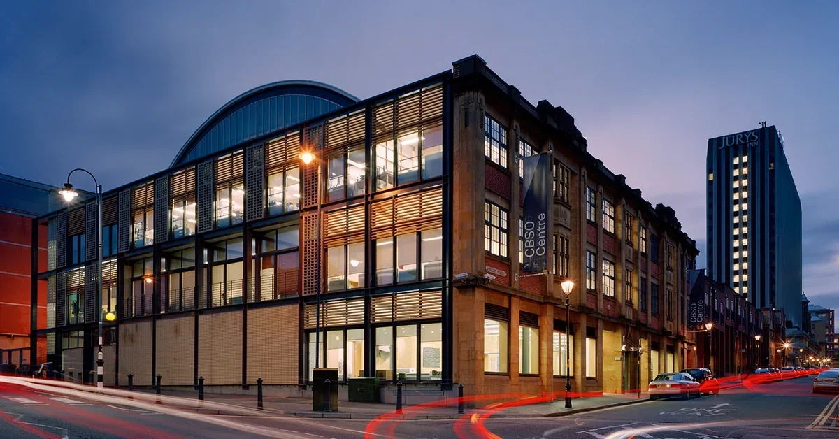 The CBSO Centre building in Birmingham, lit up at dusk, with light-trails from passing traffic on the street outside.